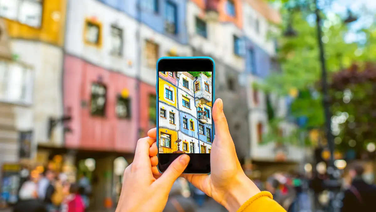 Ein Bild in dem ein Smartphone ein Hundertwasser-Haus in Wien fotografiert.
