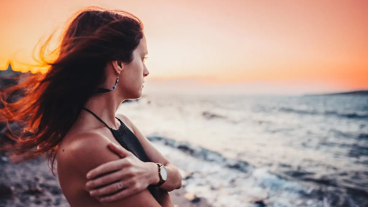 Eine Frau blickt am Strand melancholisch in die Ferne.
