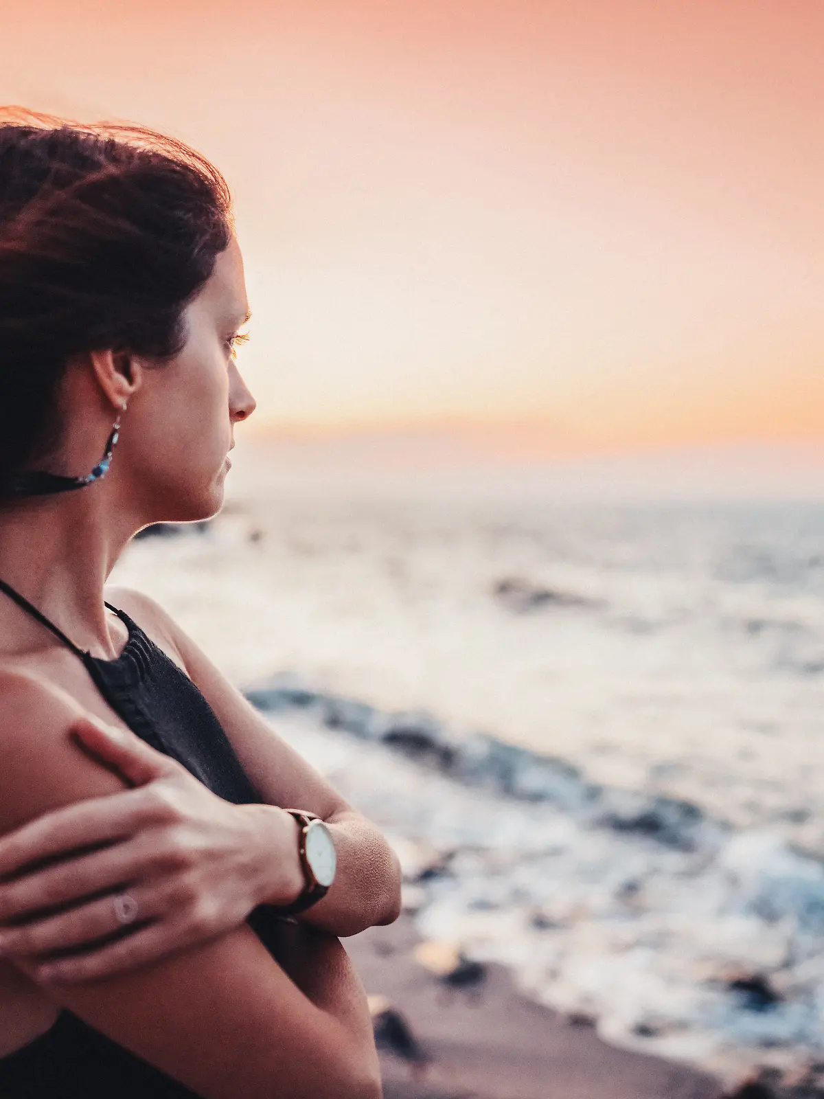 Eine Frau blickt am Strand melancholisch in die Ferne.