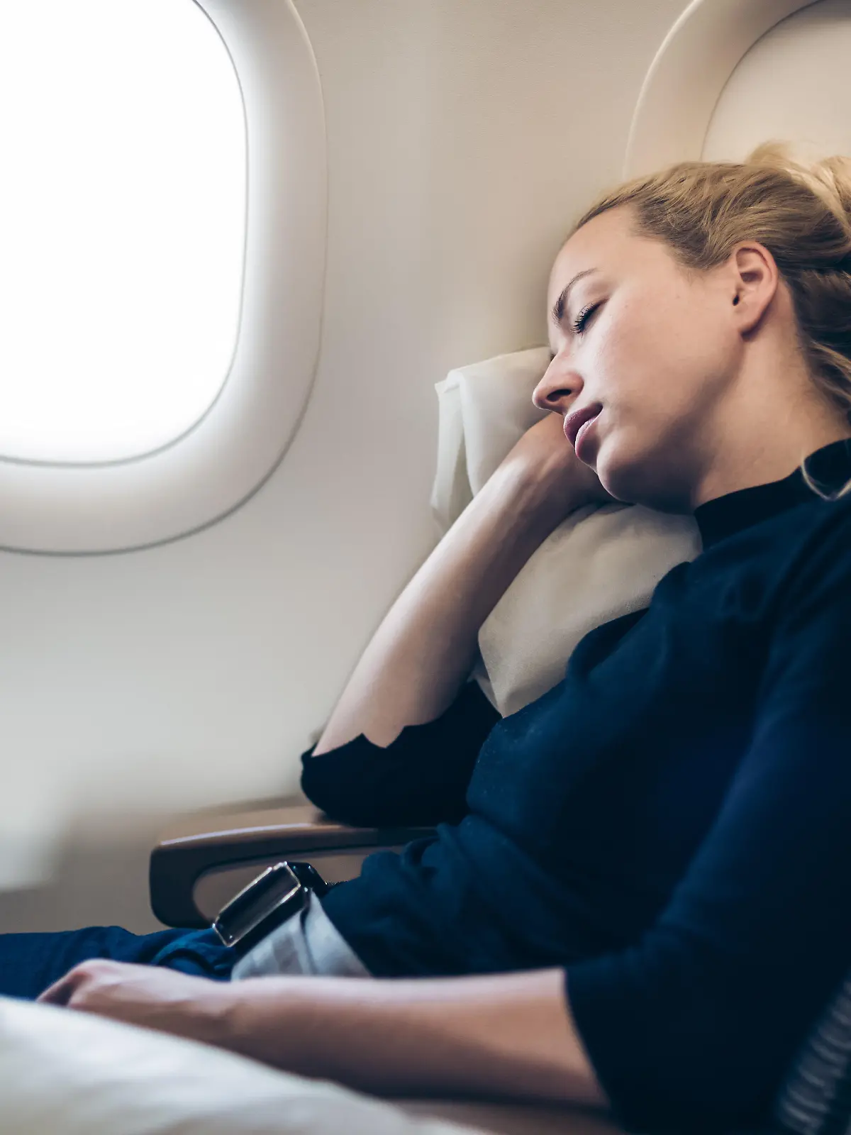 Frau lehnt mit geschlossenen Augen an Flugzeugwand.
