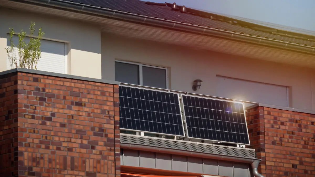 Modern residential building with solar panels on a balcony railing and on roof with sunlight reflection and special lens flare light effect.