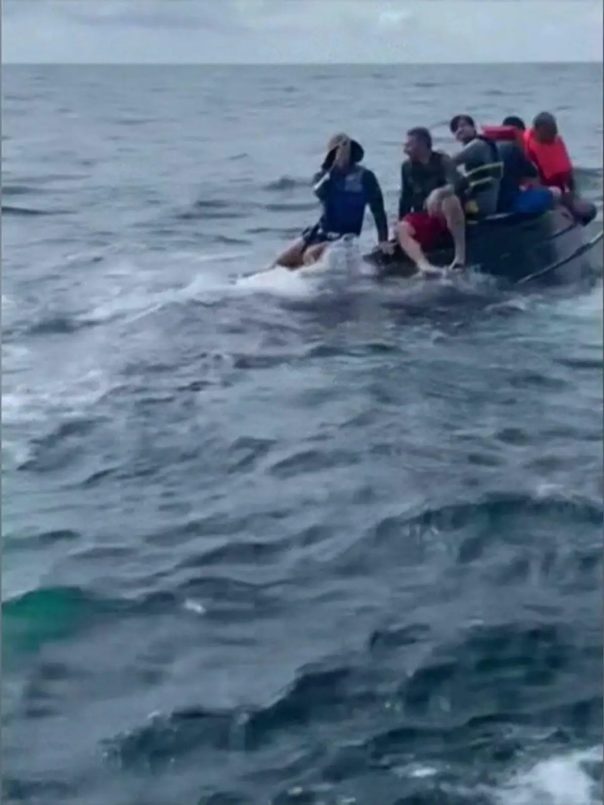 Bild zu: "Fünf Angler kauern auf gekentertem Boot im Meer "