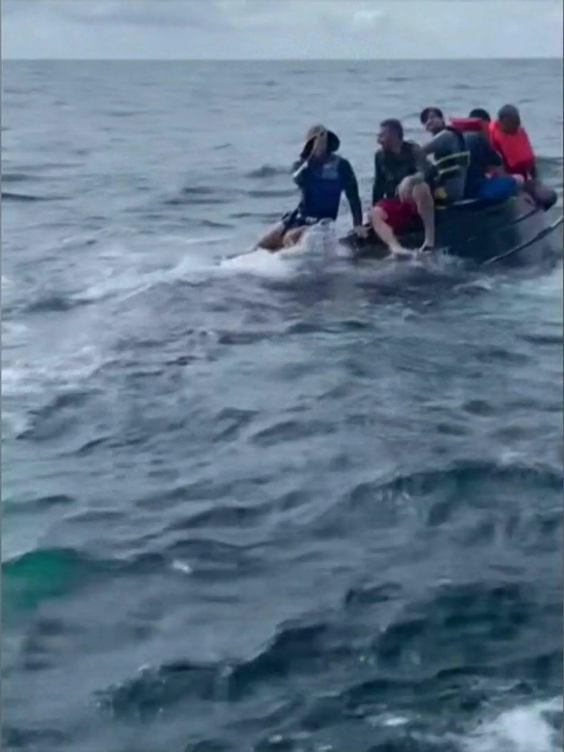 Bild zu: "Fünf Angler kauern auf gekentertem Boot im Meer "