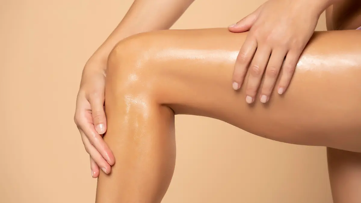 Close-up on a woman applying cream on her legs on beige background