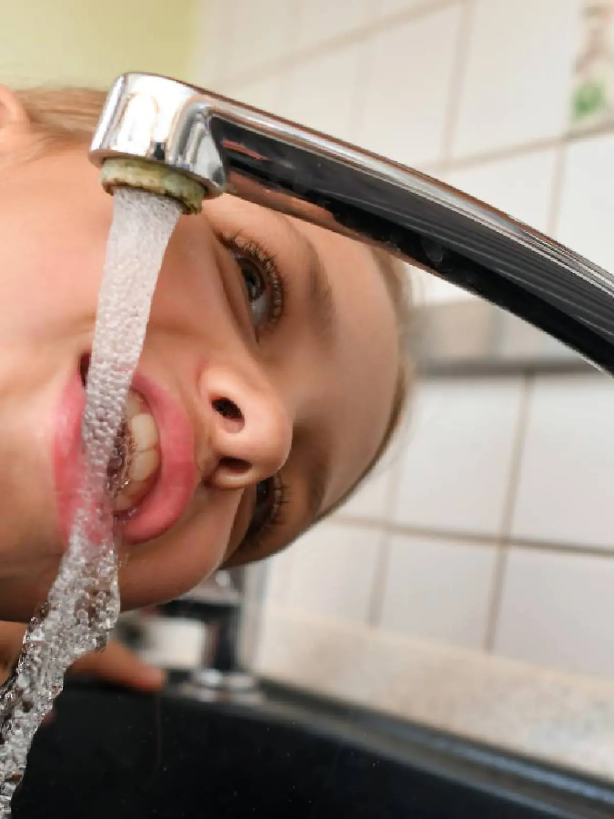 Mädchen trinkt Wasser am Wasserhahn.