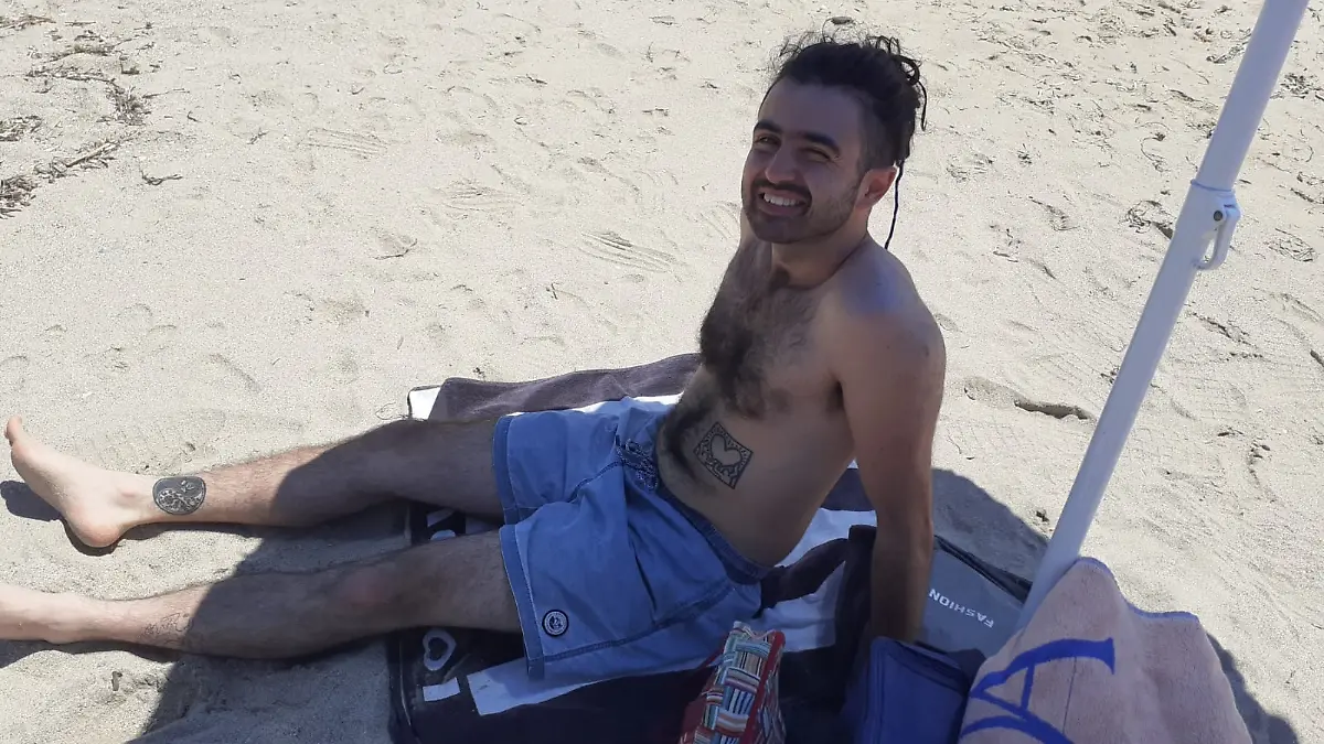 Ein Mann sitzt mit Badehose am Strand.