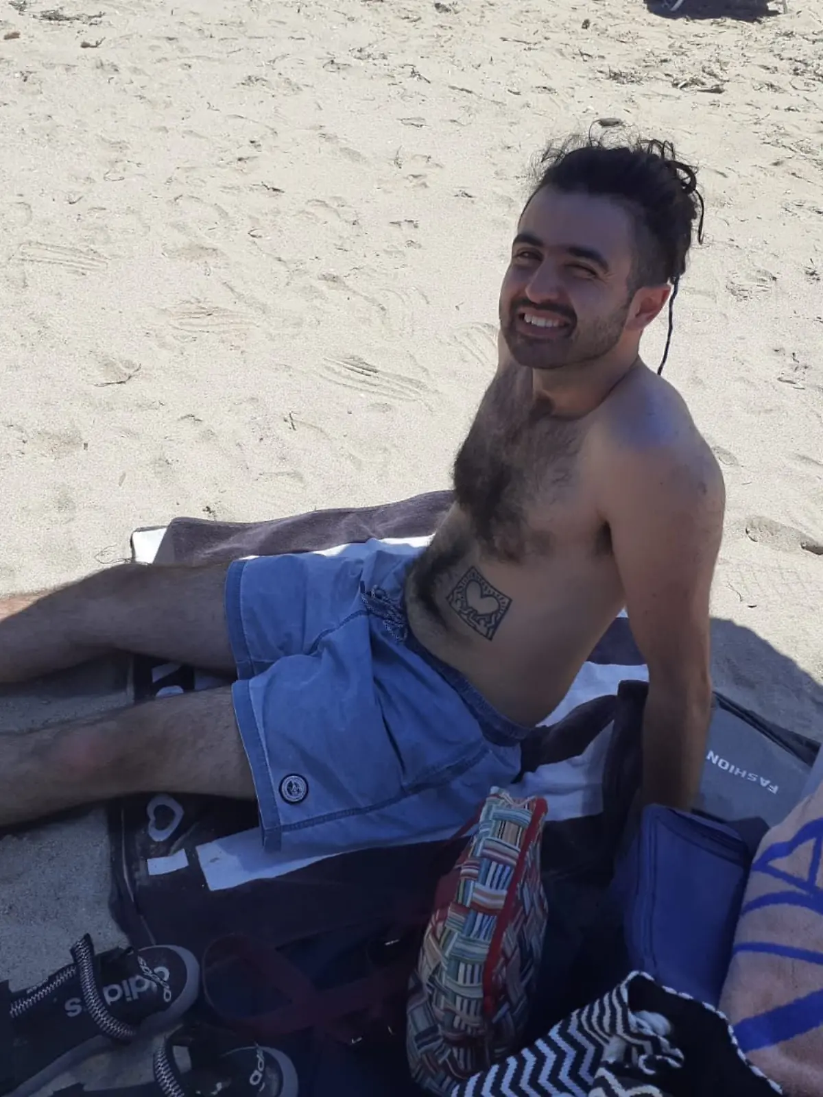 Ein Mann sitzt mit Badehose am Strand. 