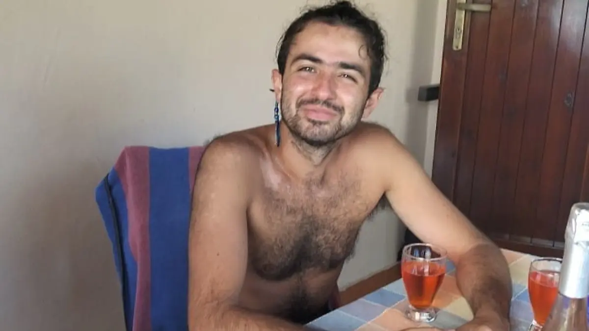 Ein junger Mann sitzt oberkörperfrei an einem Tisch.
