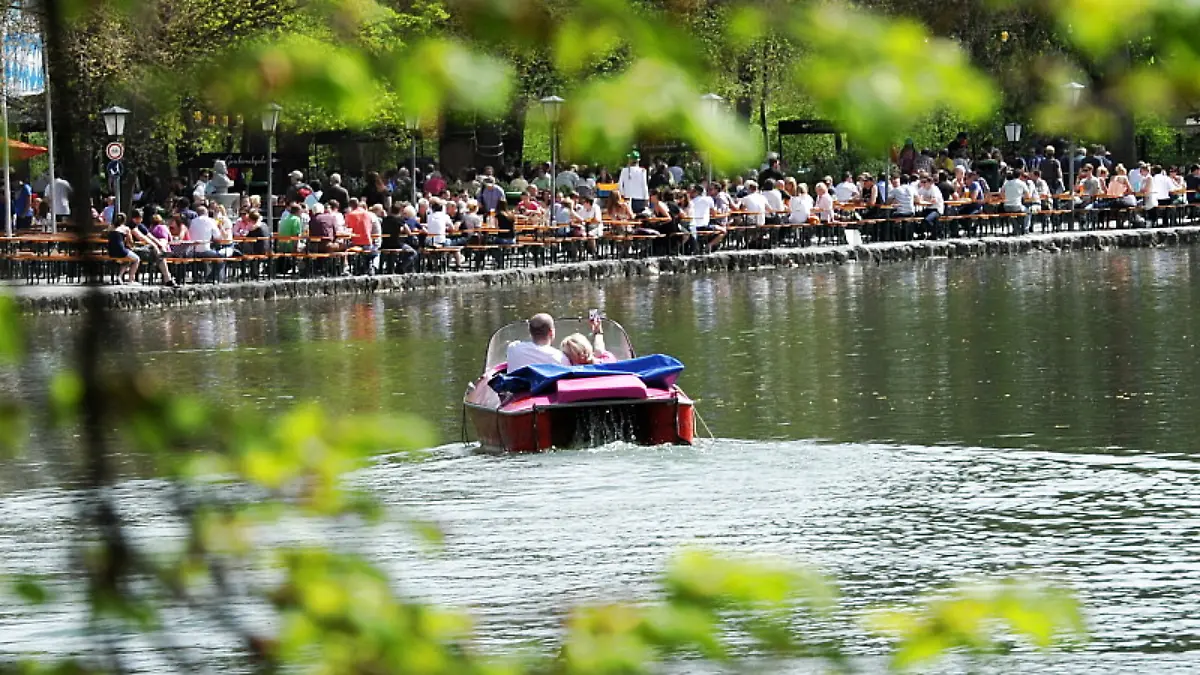 Ein Mann und eine Frau fahren am Freitag (27.04.2012) in München (Oberbayern) im Englischen Garten auf dem Kleinhesseloher See Tretboot, während dahinter der Biergarten am Seehaus schon viele Gäste hat. Das Wetter soll auch in den kommenden Tagen in weiten Teilen Bayerns sonnig und warm werden. Foto: Tobias Hase dpa/lby +++(c) dpa - Bildfunk+++