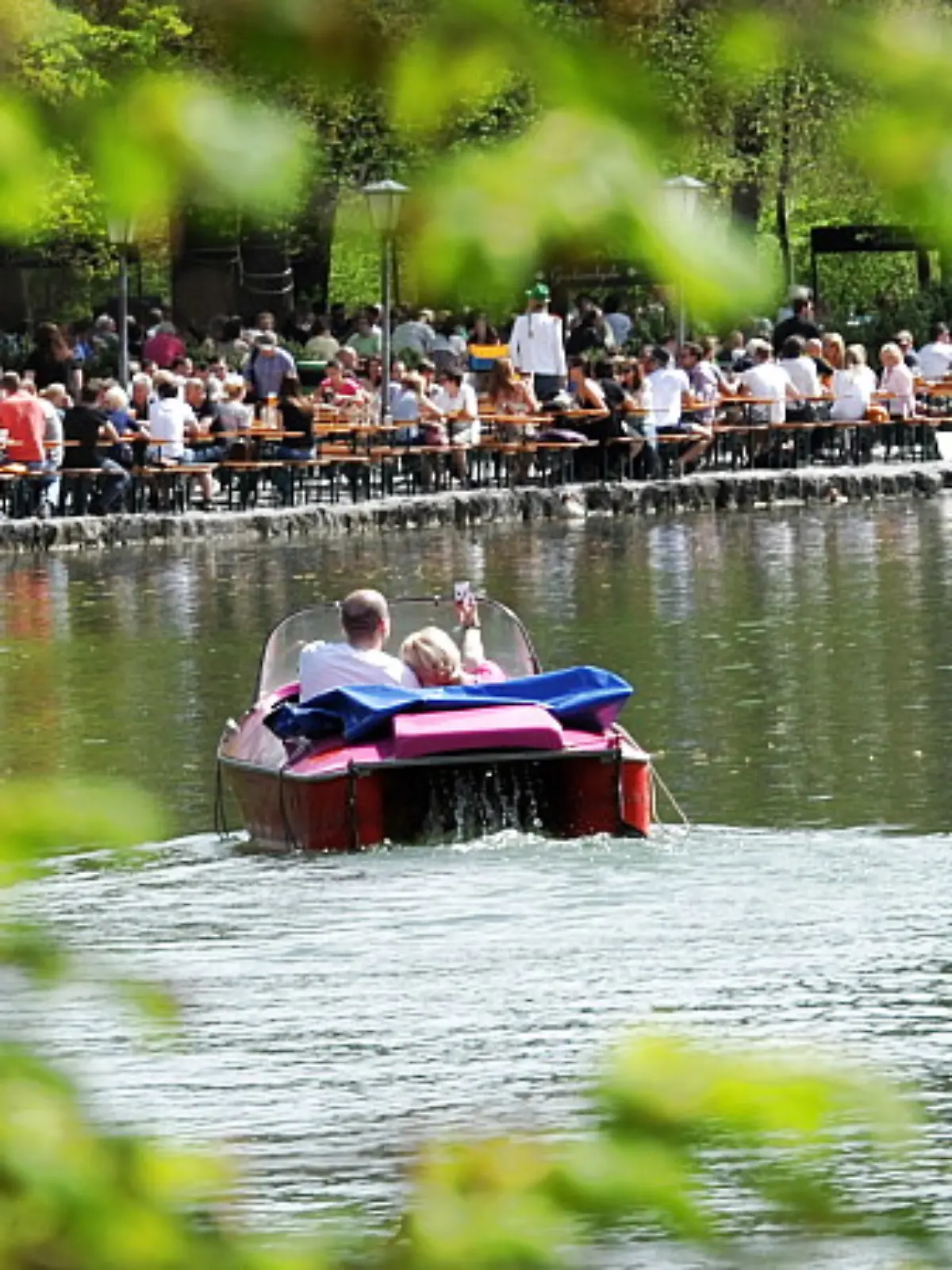 Ein Mann und eine Frau fahren am Freitag (27.04.2012) in München (Oberbayern) im Englischen Garten auf dem Kleinhesseloher See Tretboot, während dahinter der Biergarten am Seehaus schon viele Gäste hat. Das Wetter soll auch in den kommenden Tagen in weiten Teilen Bayerns sonnig und warm werden. Foto: Tobias Hase dpa/lby  +++(c) dpa - Bildfunk+++
