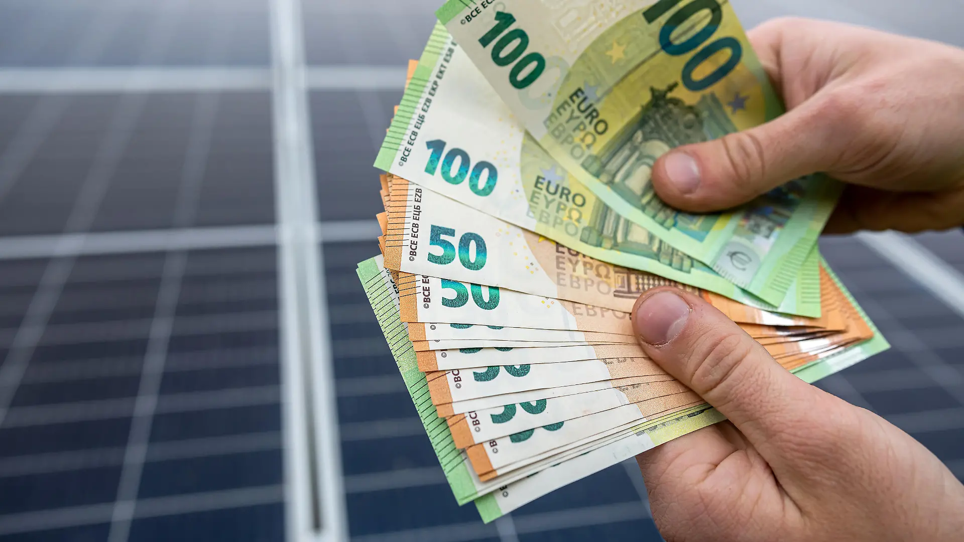 Euro-Geldscheine vor einer Solaranlage