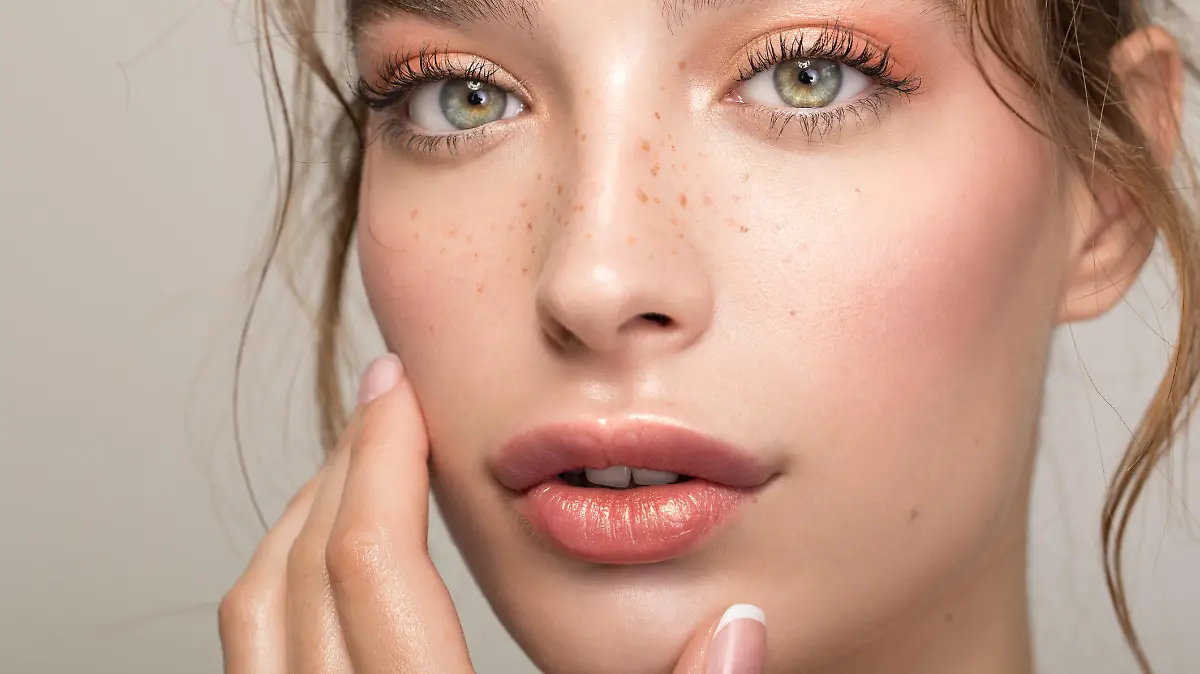 Closeup studio shot of a beautiful young woman with freckles skin posing against a grey background