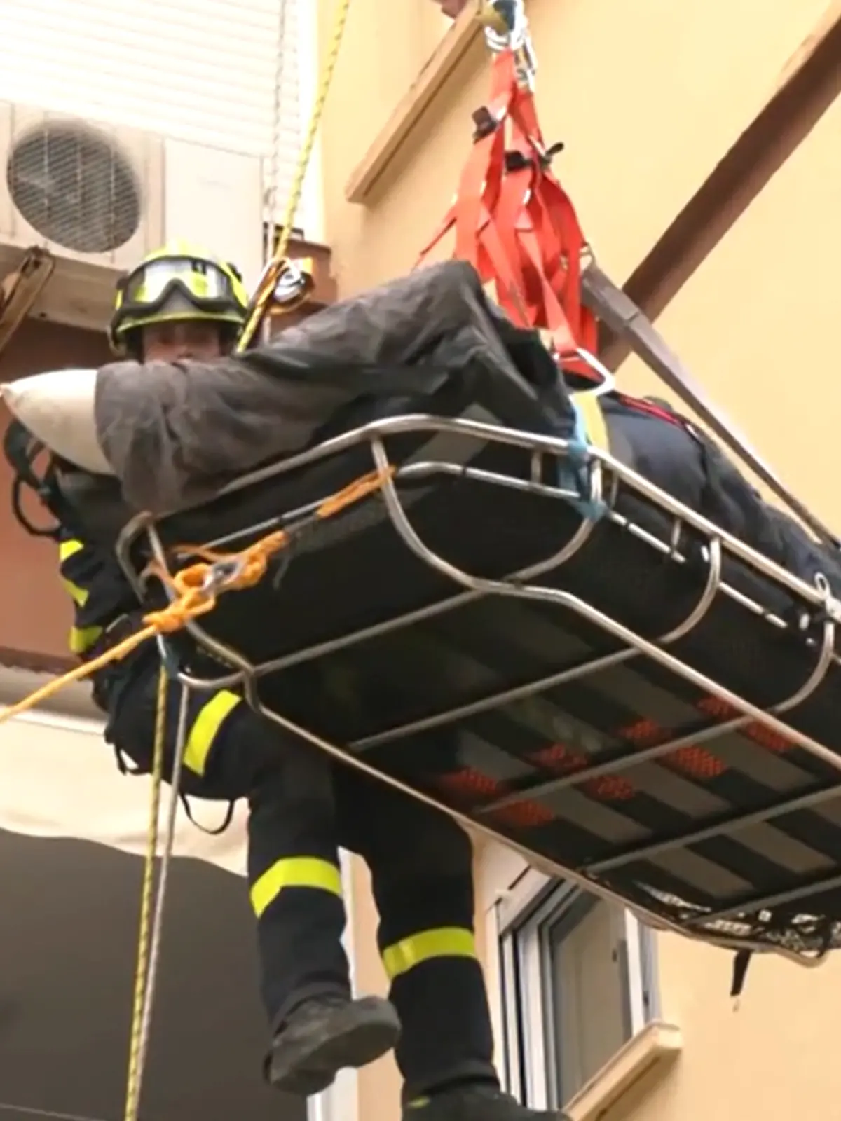 Feuerwehrkräfte bergen einen sehr schweren Mann mit einem Kran über einen Balkon.