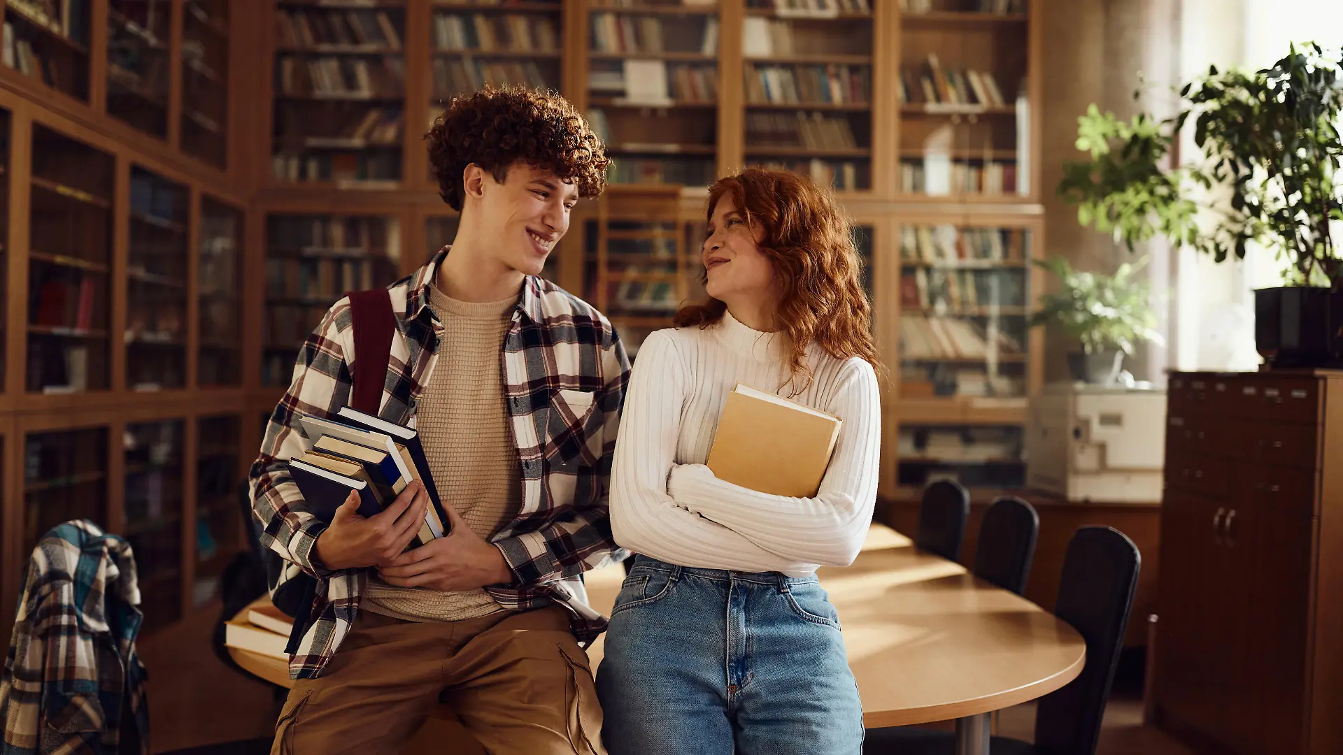 Junger Mann und junge Frau lächeln sich an in einer Bibliothek.