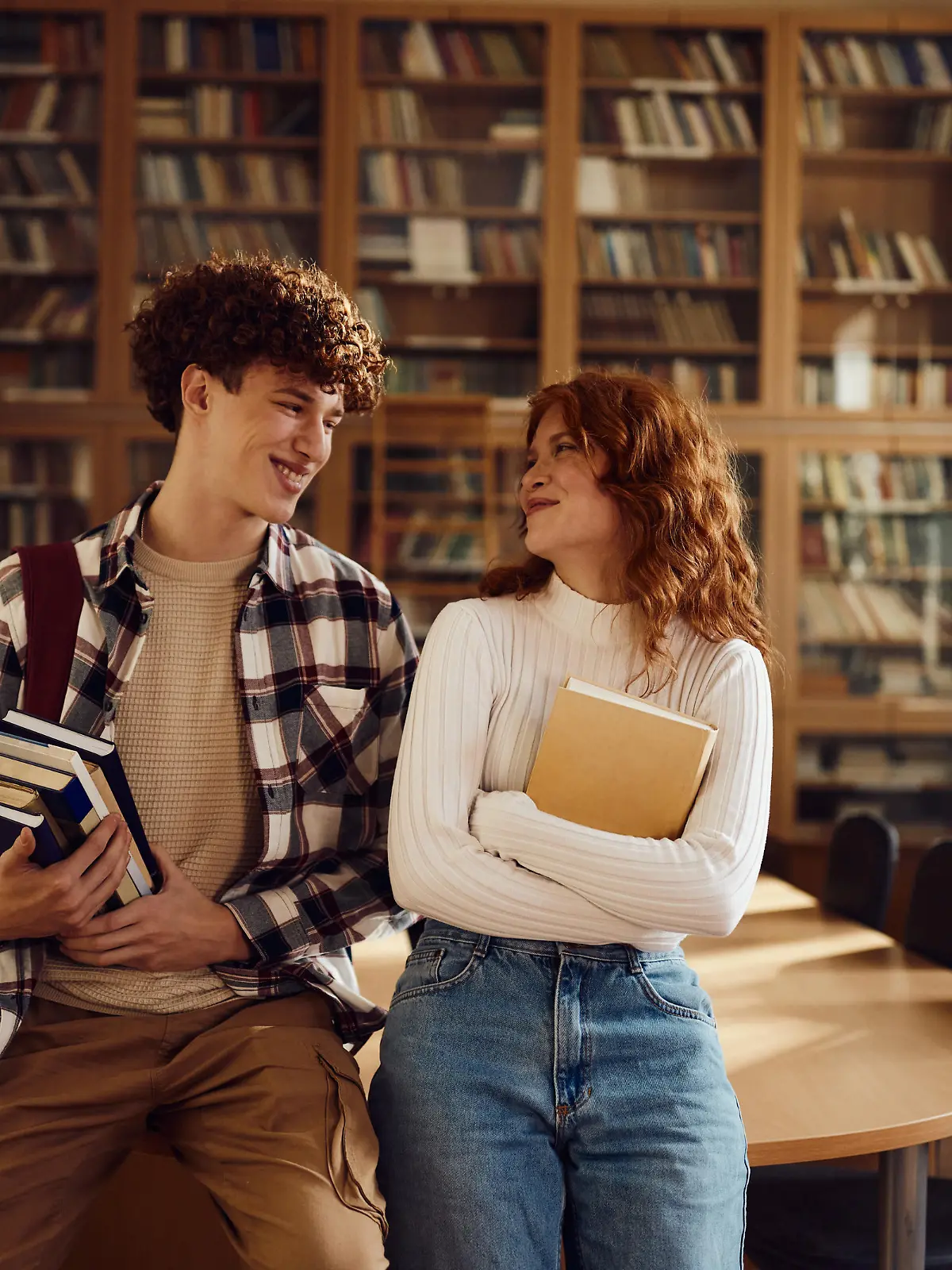 Junger Mann und junge Frau lächeln sich an in einer Bibliothek.