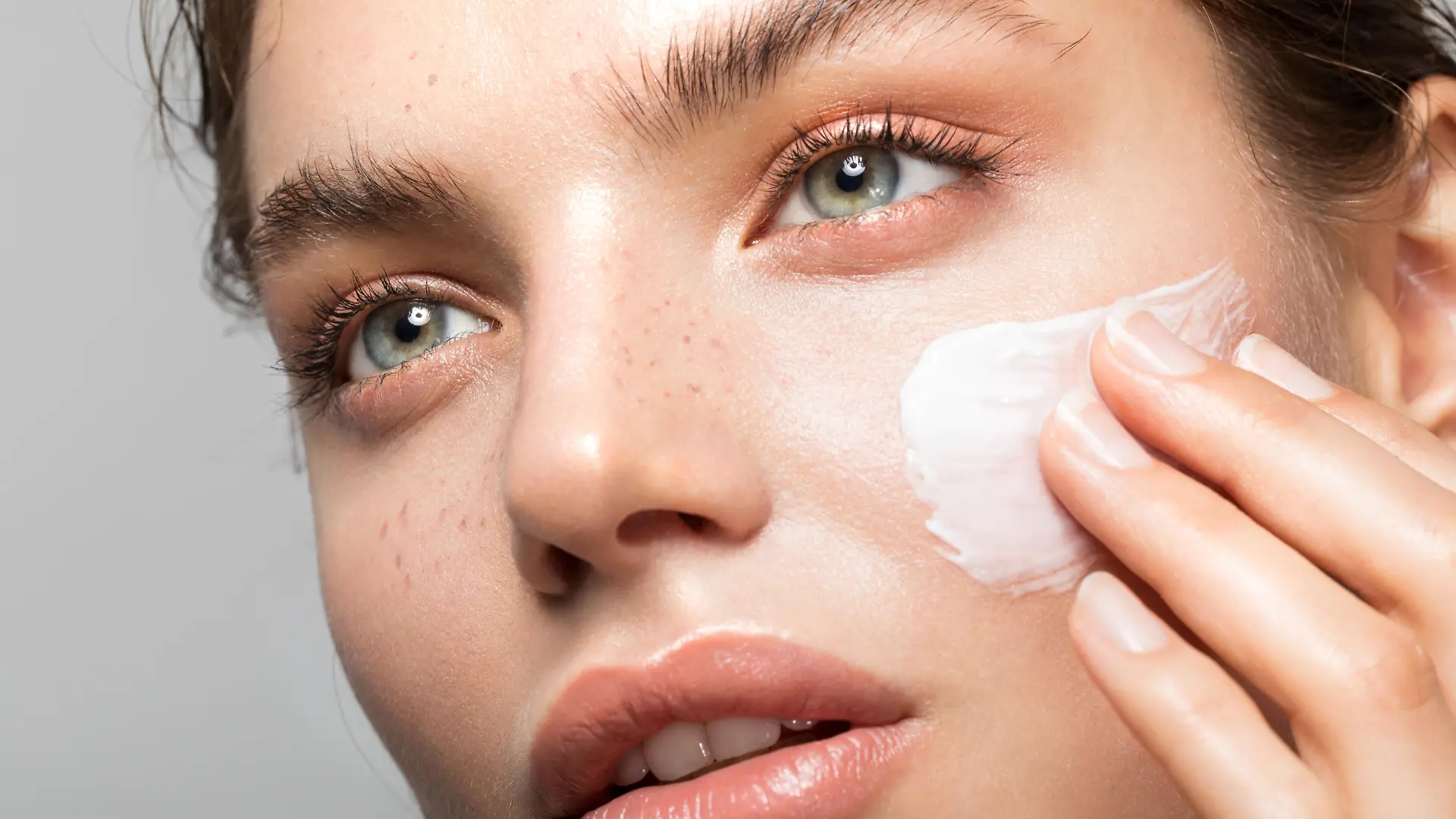 Close up studio shot of a beautiful woman with perfect skin, applying moisturizing cream