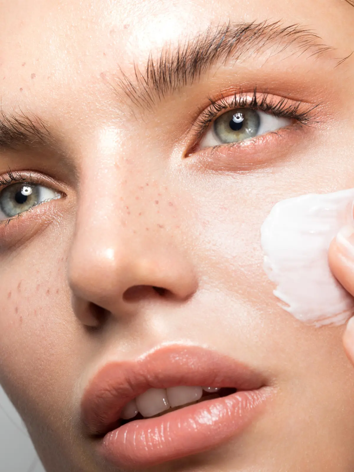 Close up studio shot of a beautiful woman with perfect skin, applying moisturizing cream
