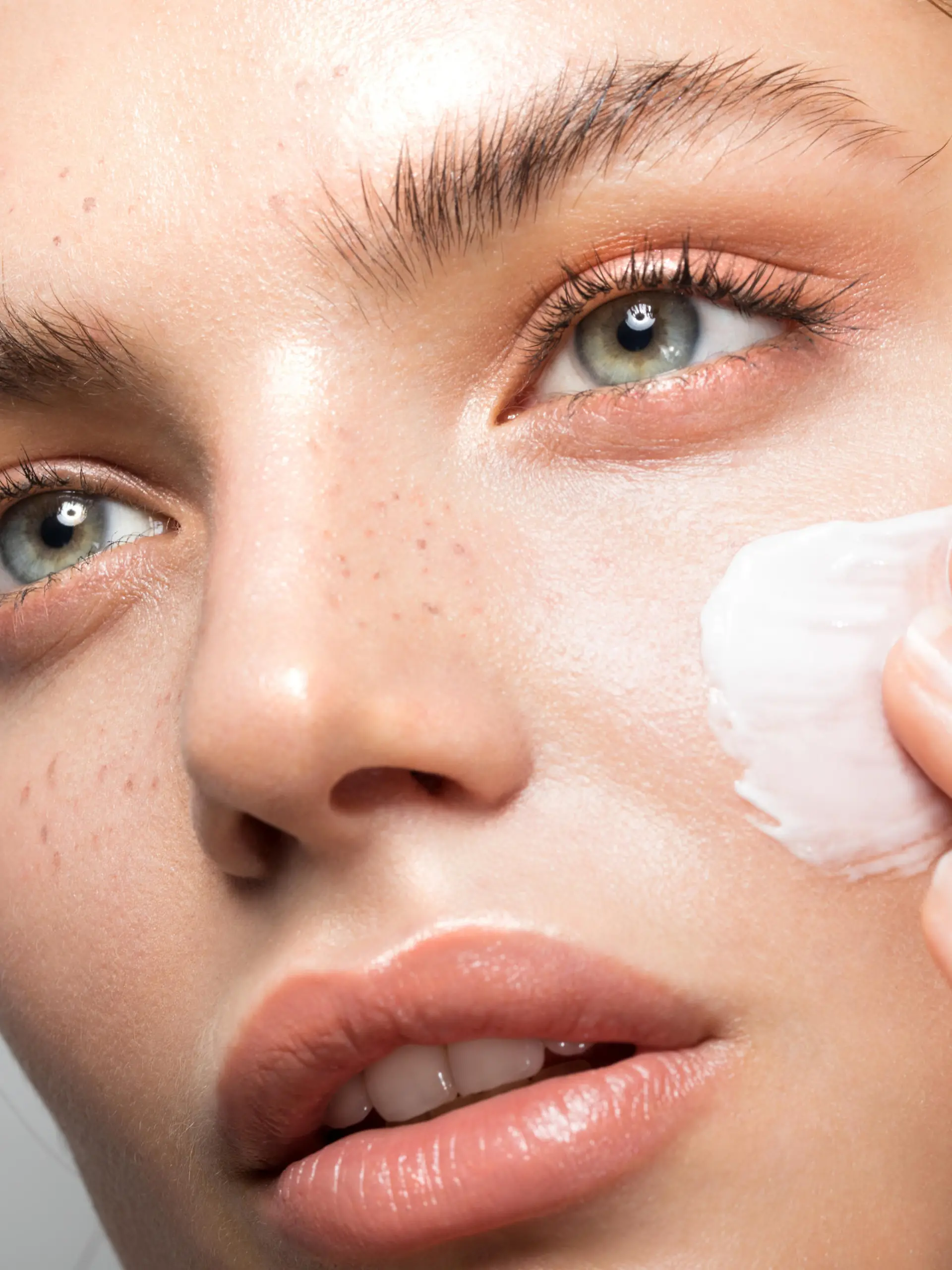 Close up studio shot of a beautiful woman with perfect skin, applying moisturizing cream