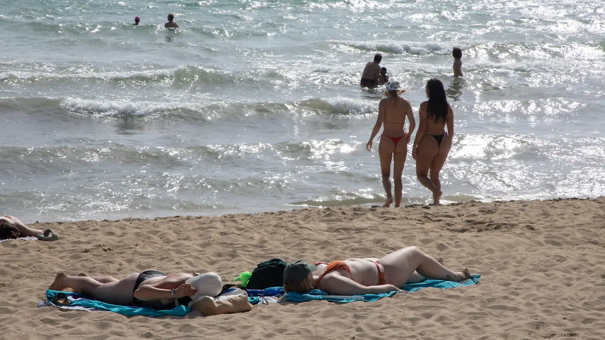 Menschen sonnen sich, baden und spazieren am Strand von Arenal.