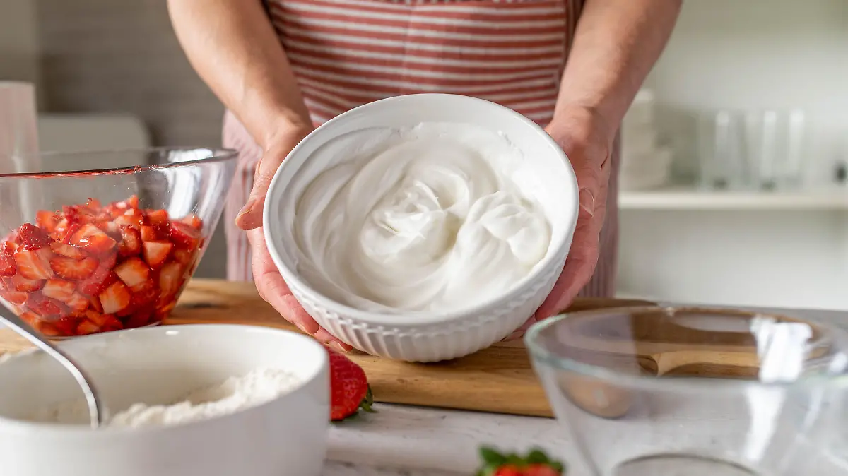 Bowl with fresh whipped egg white holding by woman´s hand in the kitchen. Front view