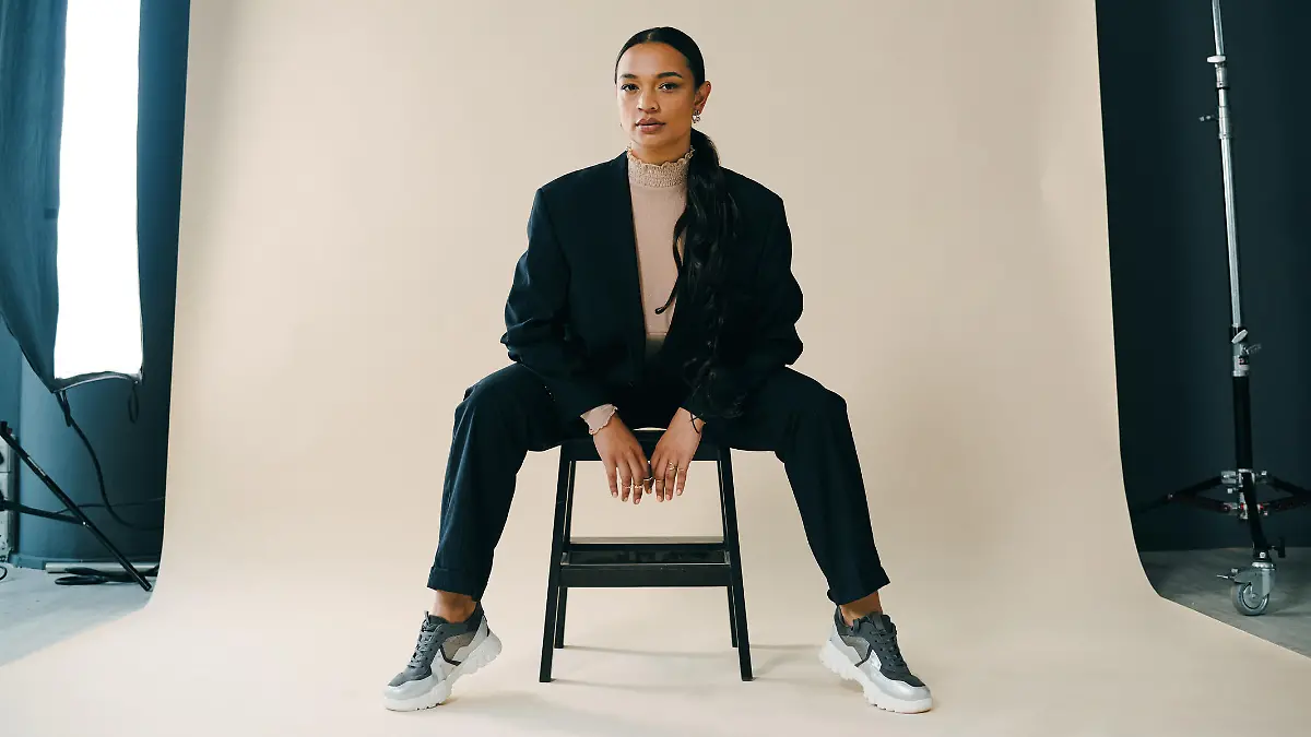Studio portrait of a beautiful young woman sitting on a chair during a photoshoot against a brown background