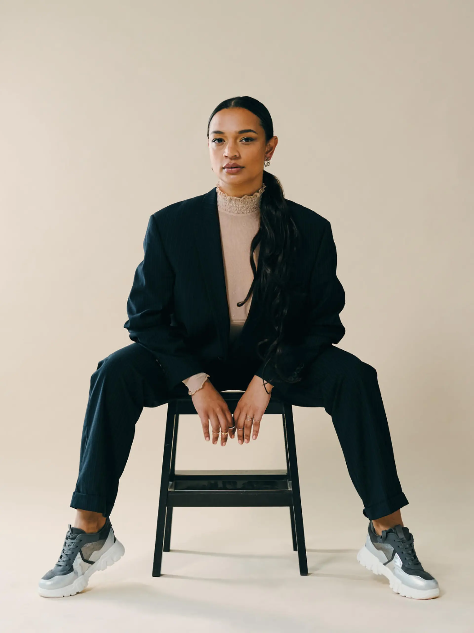 Studio portrait of a beautiful young woman sitting on a chair during a photoshoot against a brown background