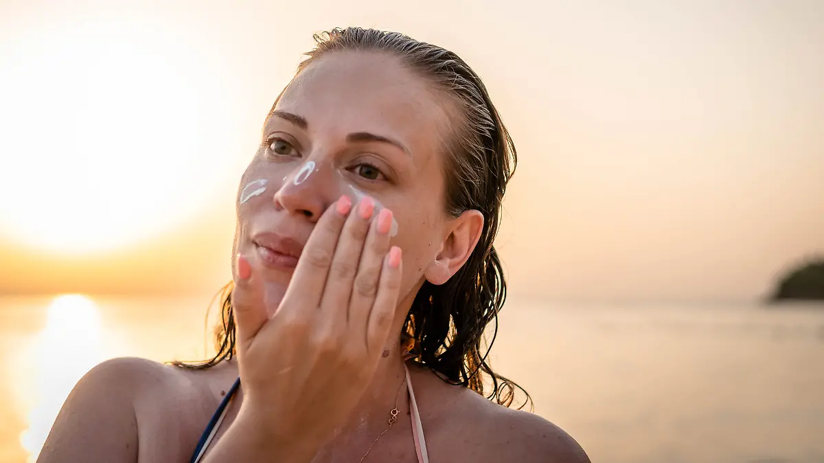 Eine Frau cremt sich am Strand das Gesicht ein.