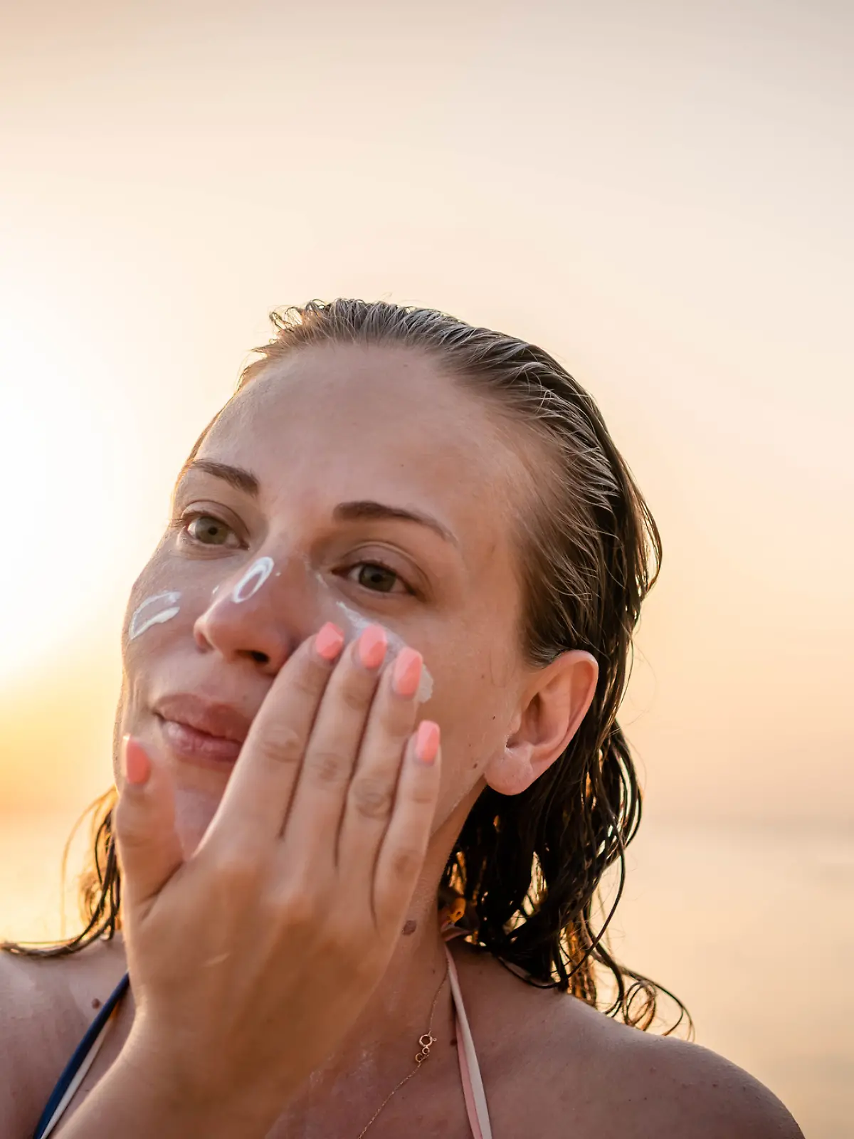 Eine Frau cremt sich am Strand das Gesicht ein.