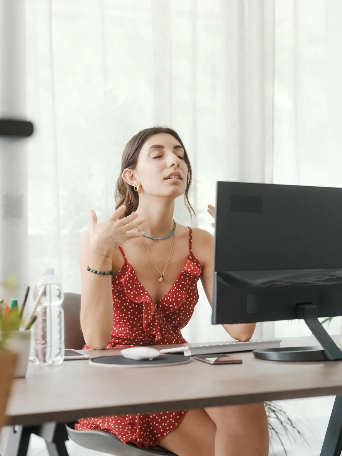 Woman sitting at desk at home during a summer heat wave, she is cooling herself with an electric fan