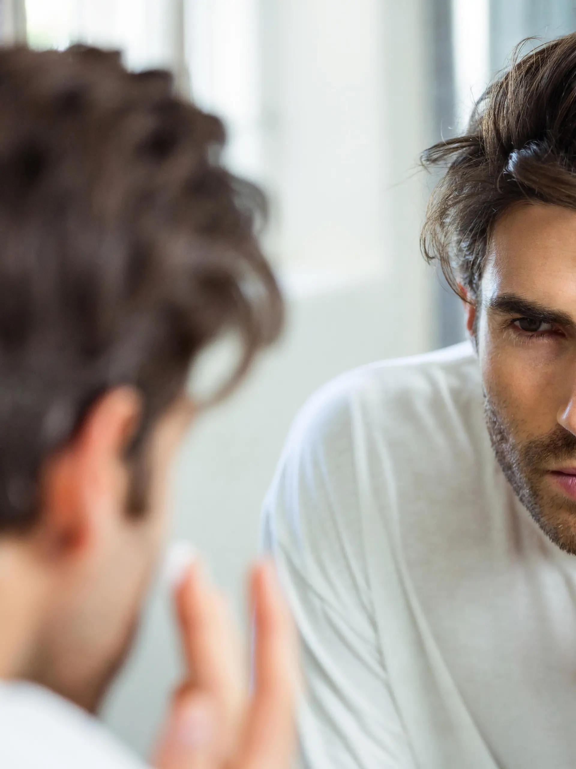 Reflection of young man in bathroom mirror applying moisturizer on his face