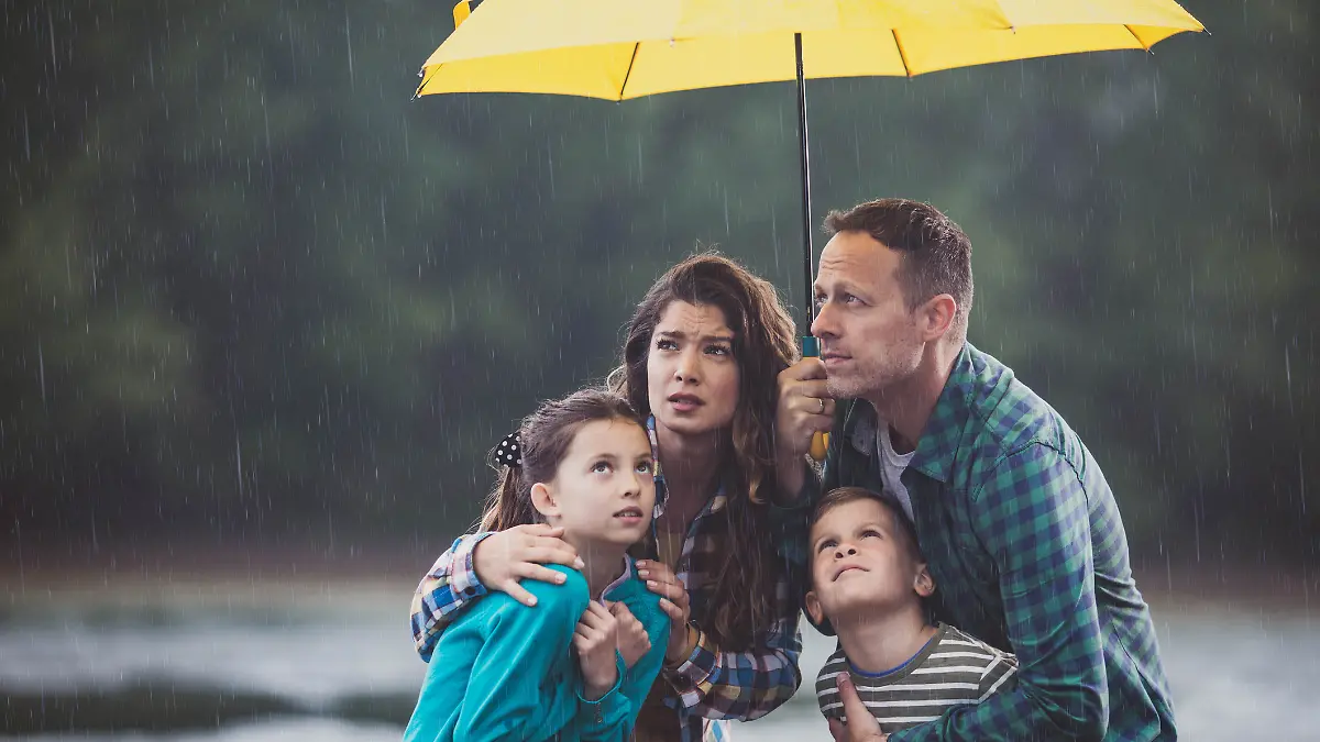Familie steht unter einem Schirm im Regen.