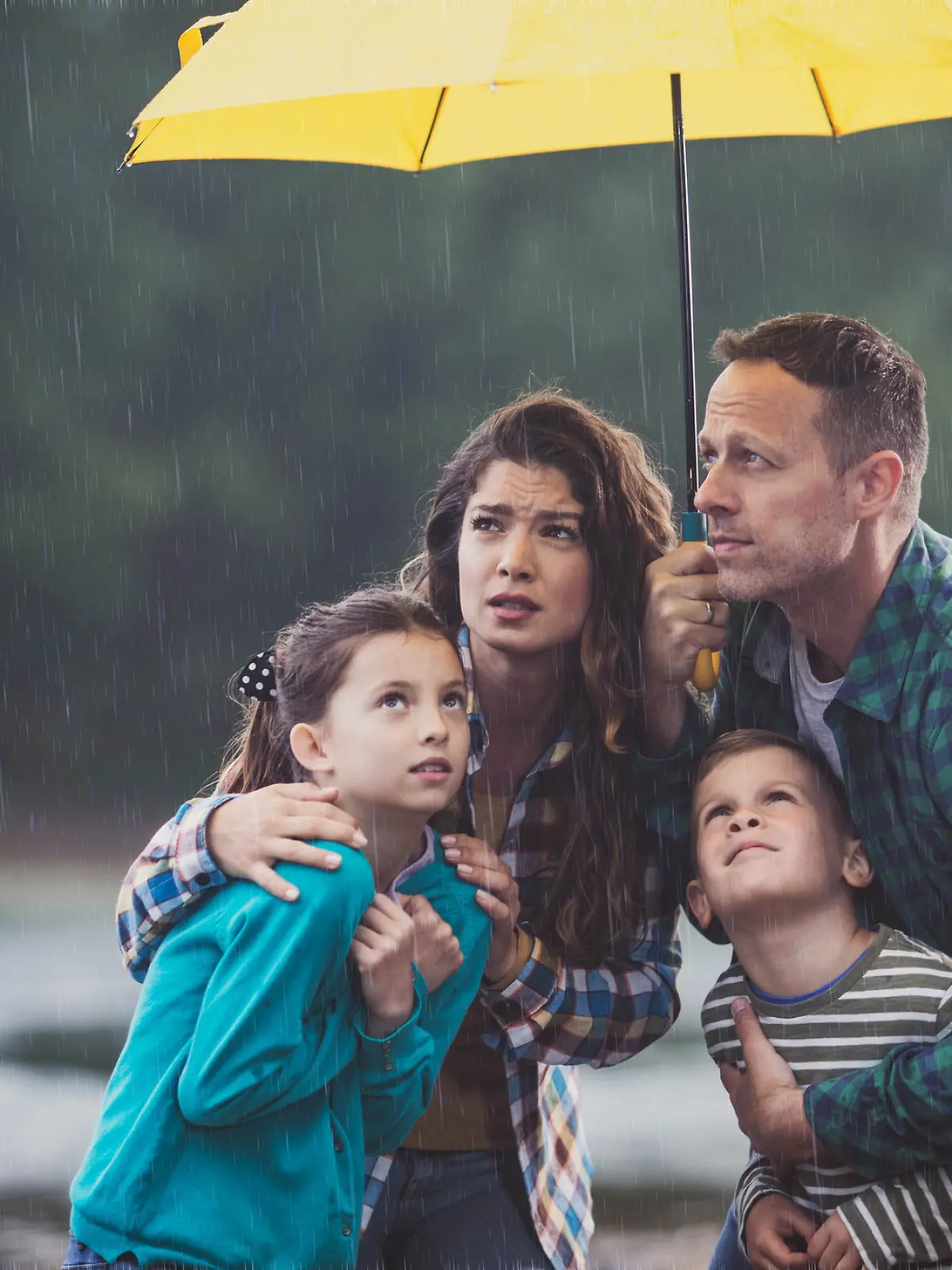 Familie steht unter einem Schirm im Regen.