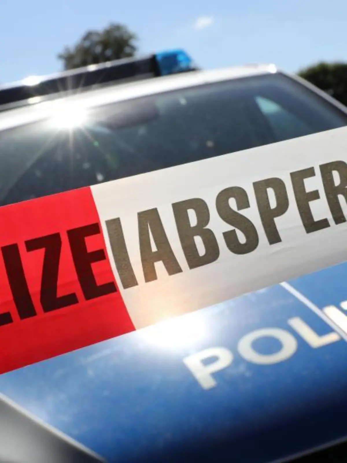 Eine Polizeiabsperrung hängt vor einem Polizeiauto