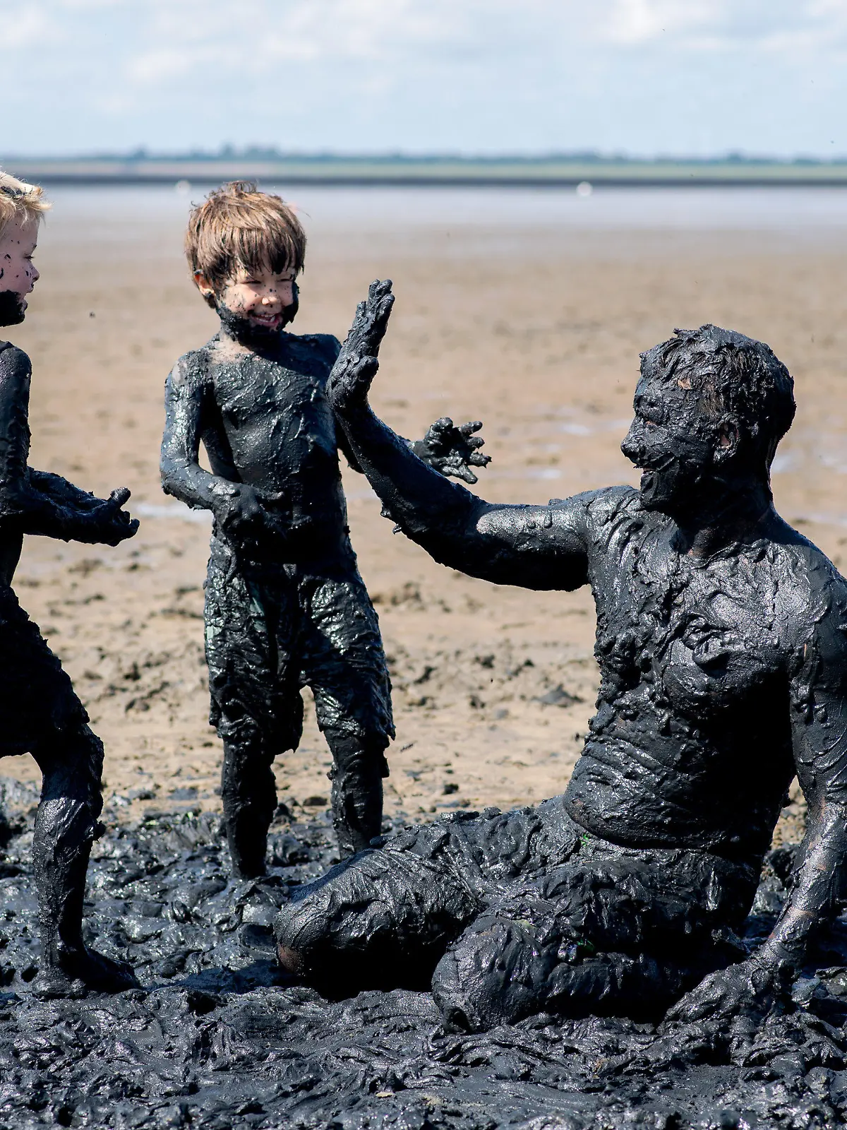 dpatopbilder - 28.07.2024, Niedersachsen, Dangast: Paul (l-r), Leon, und Arne aus Oldenburg spielen bei sonnigem Wetter bei Ebbe im Schlick am Strand von Dangast. Foto: Hauke-Christian Dittrich/dpa - ACHTUNG: Nur zur redaktionellen Verwendung im Zusammenhang mit der aktuellen Berichterstattung +++ dpa-Bildfunk +++