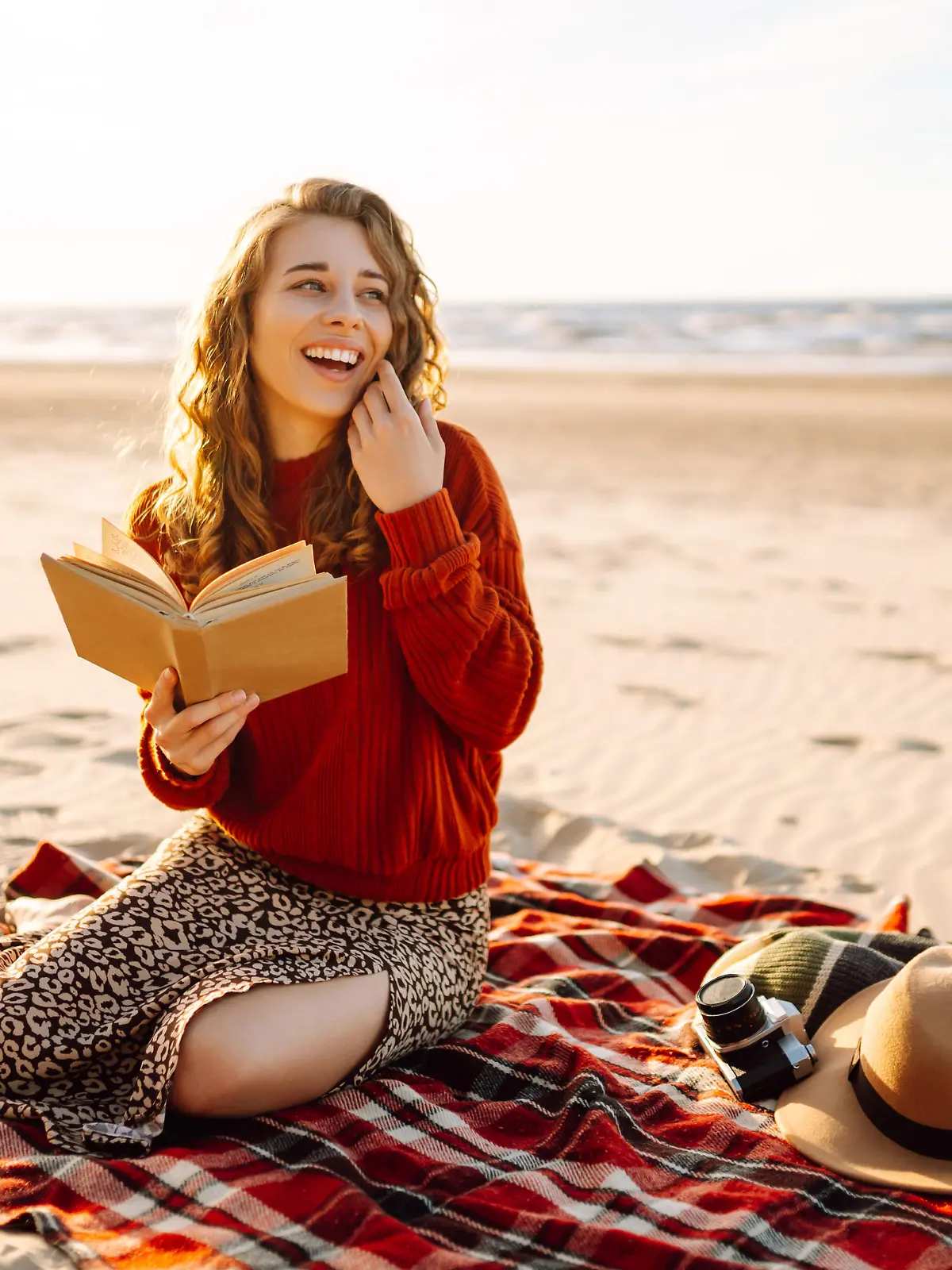 Beautiful woman sitting on the blanket reading a book at the beach picnic. The concept of relaxation, enjoyment, solitude with nature.