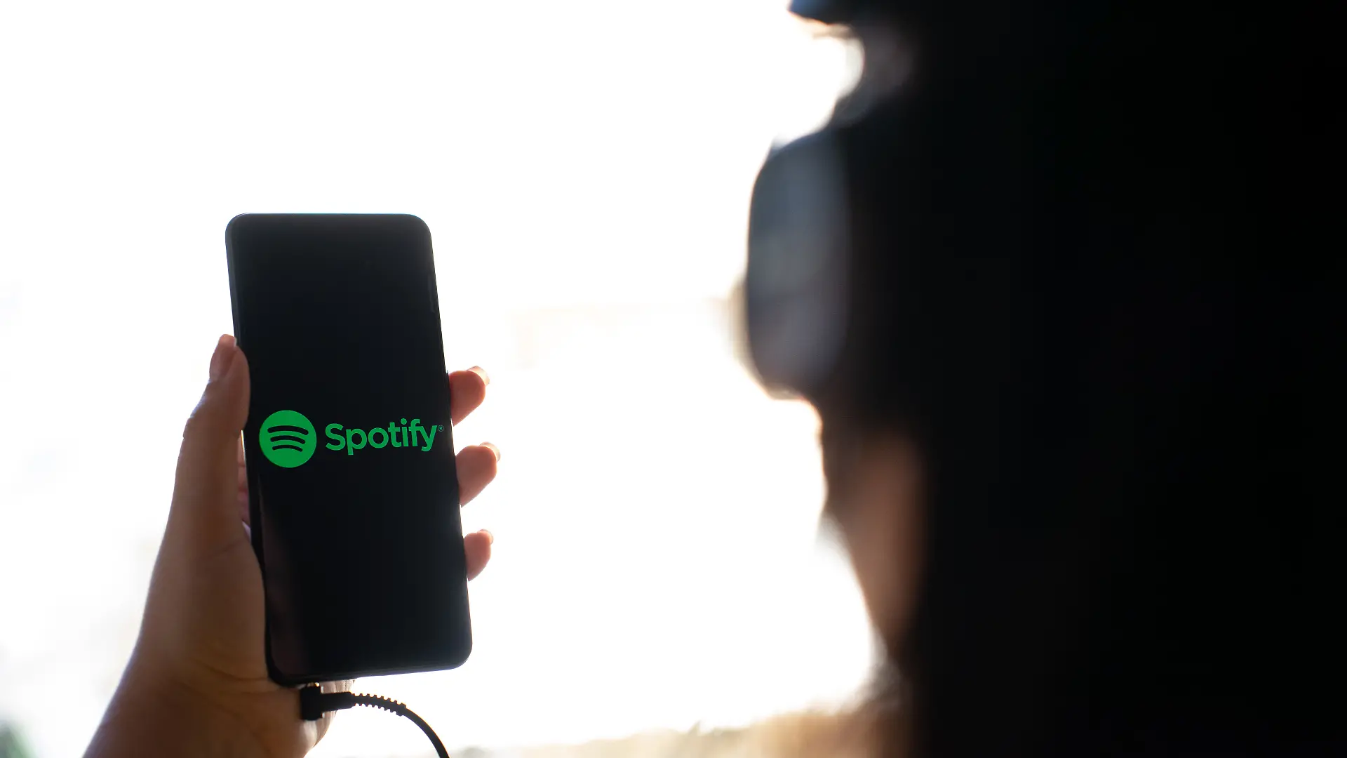 A woman holding a mobile phone with the logo of Spotify on its screen. (Photo by Nikos Pekiaridis/NurPhoto)