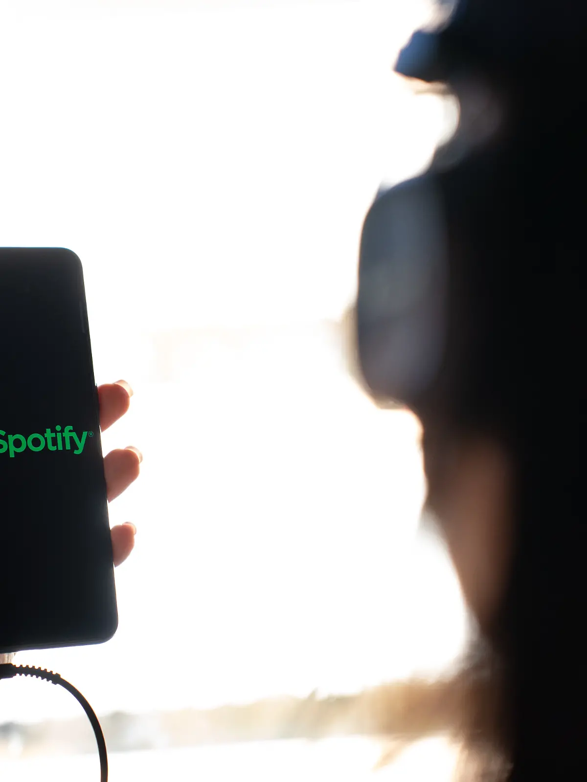 A woman holding a mobile phone with the logo of Spotify on its screen. (Photo by Nikos Pekiaridis/NurPhoto)