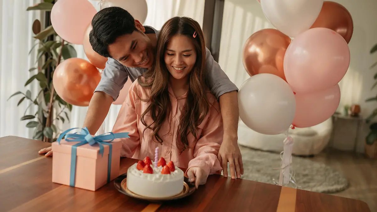 Mid-adult man hugs his wife as they celebrate her birthday with a cake and present.