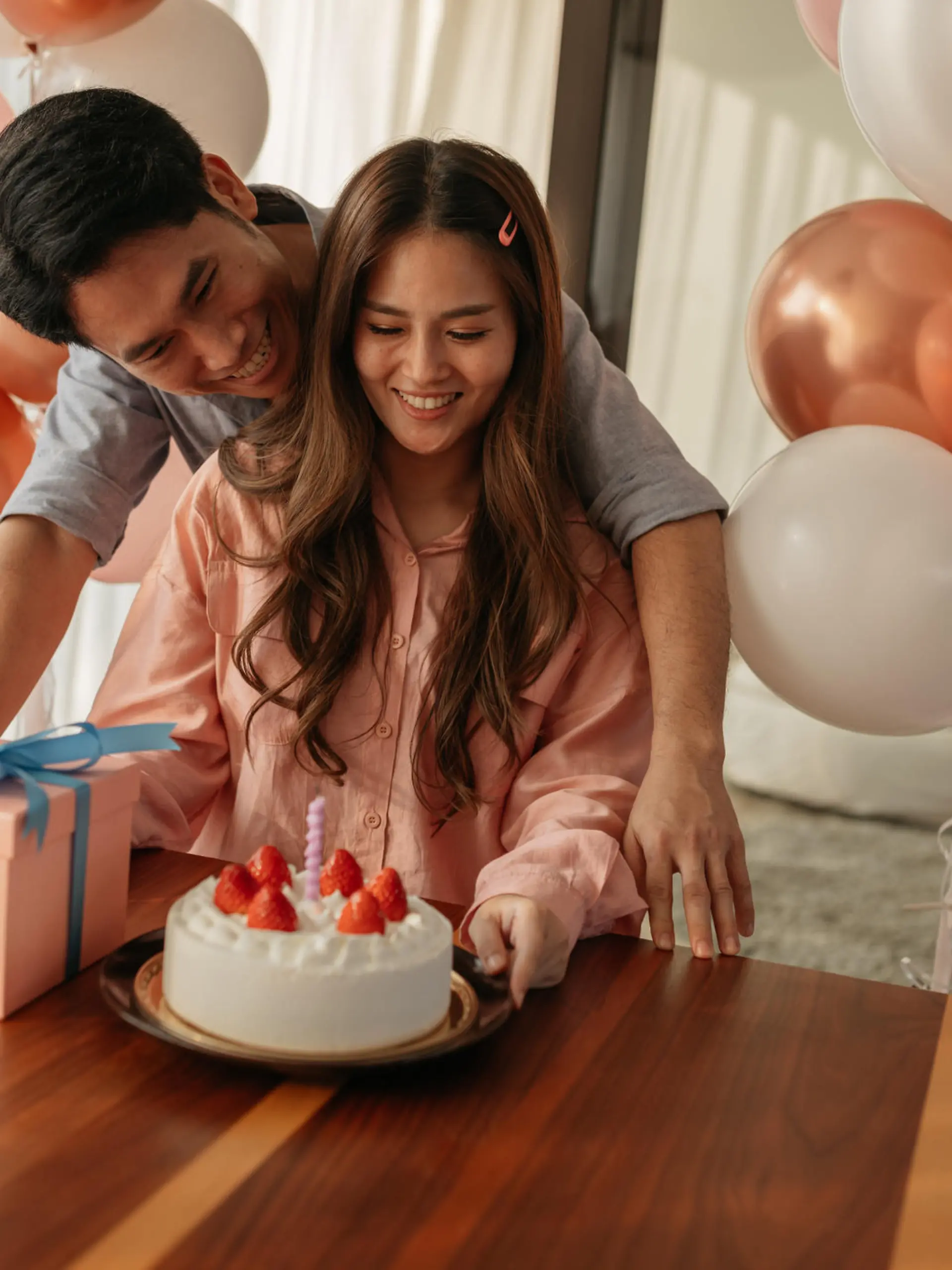 Mid-adult man hugs his wife as they celebrate her birthday with a cake and present.