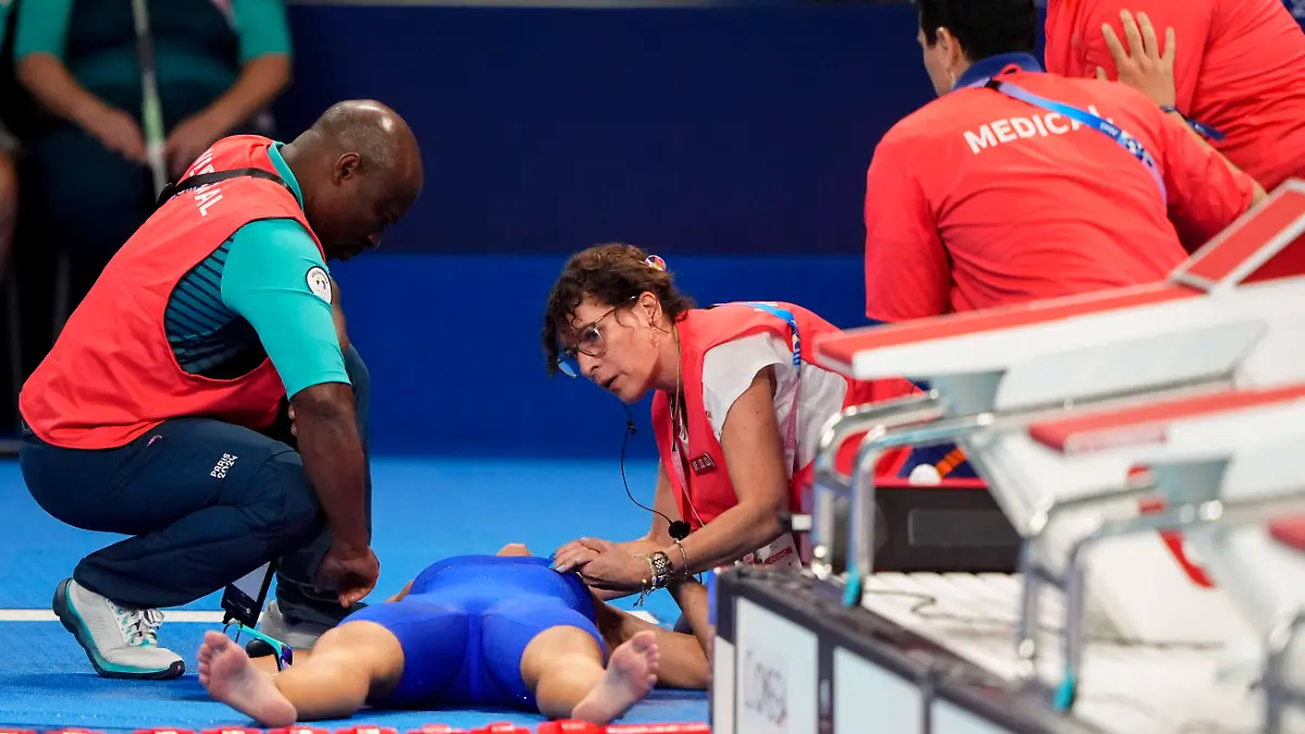Bilder aus der Schwimmhalle zeigen die Sportlerin zwischen mehreren Sanitätern.