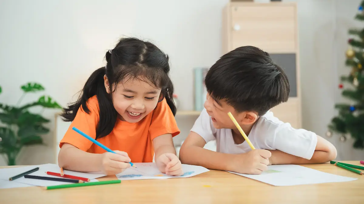 Two children are sitting at a table, drawing and smiling. Concept of joy and creativity, as the children are engaged in a fun activity together