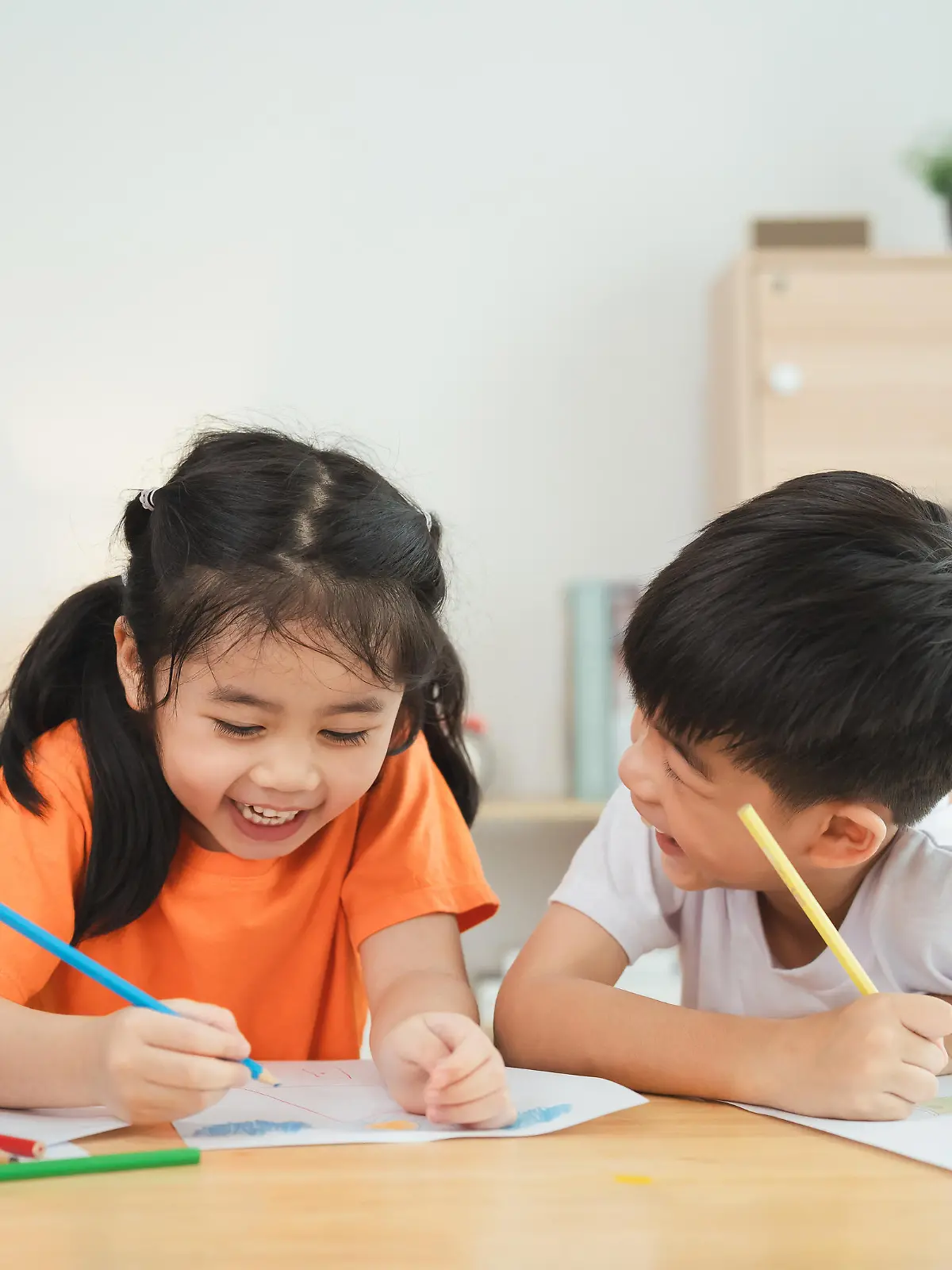 Two children are sitting at a table, drawing and smiling. Concept of joy and creativity, as the children are engaged in a fun activity together