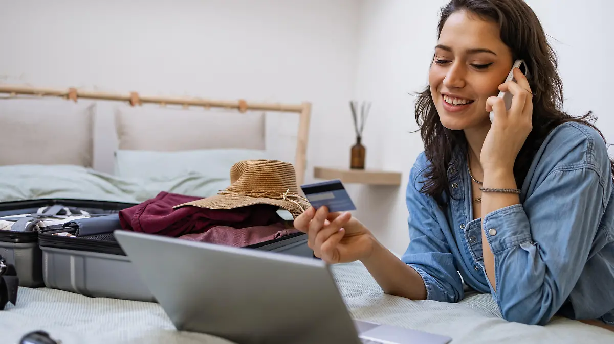 Happy woman talking won the phone phone and using laptop to make flight reservation
