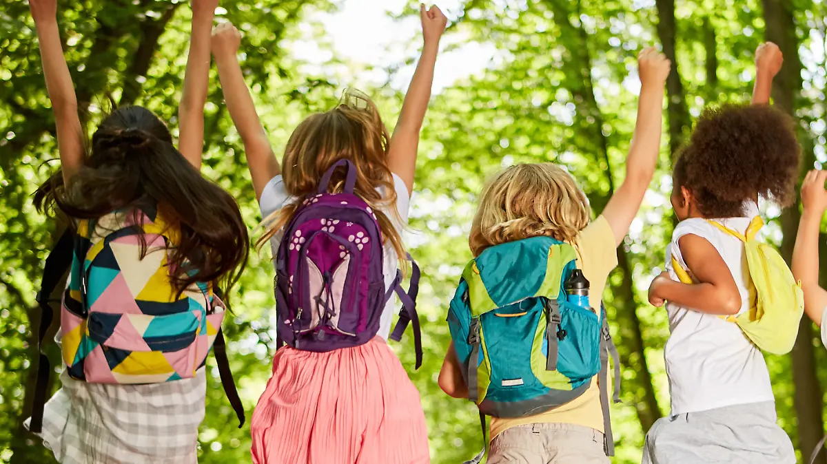 Gruppe Kinder mit Rucksäcken in der Natur im Sommer springt in die Luft