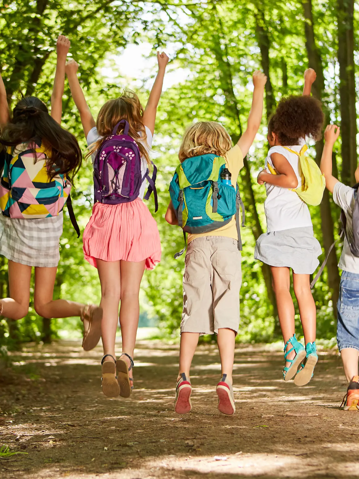 Gruppe Kinder mit Rucksäcken in der Natur im Sommer springt in die Luft