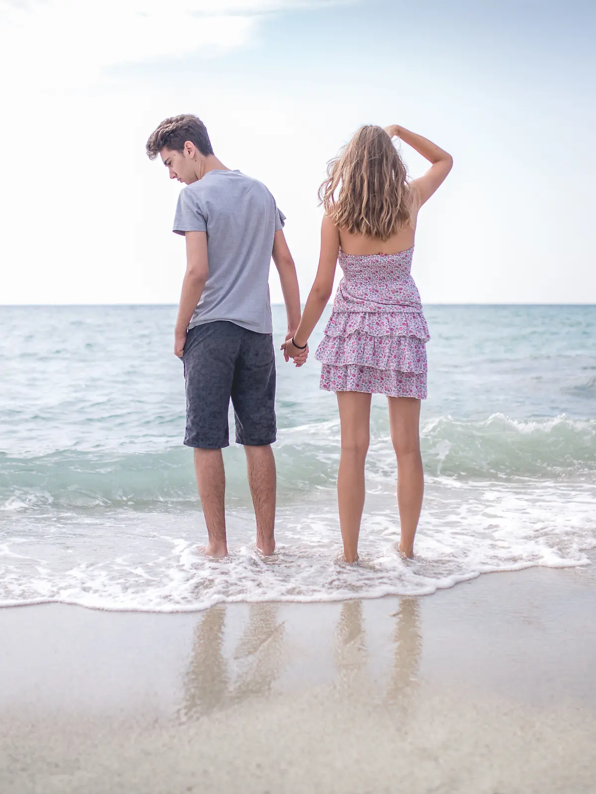 Ein Paar steht im Urlaub am Strand im Meer und scheint sichtlich schlecht gelaunt zu sein, als ob sie vorher Streit hatten.