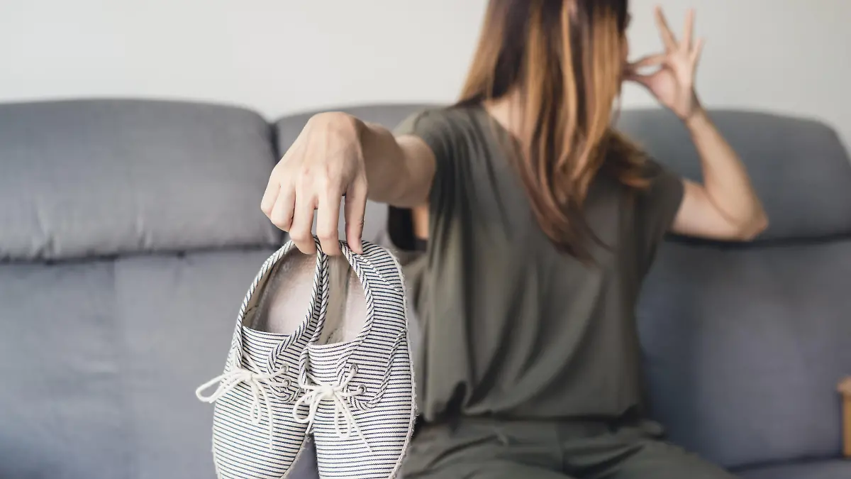 Young asian woman holding a pair of smelly and stinky shoes at home