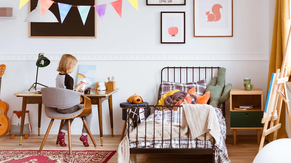 Cute little girl sitting at desk in her stylish vintage bedroom with workspace