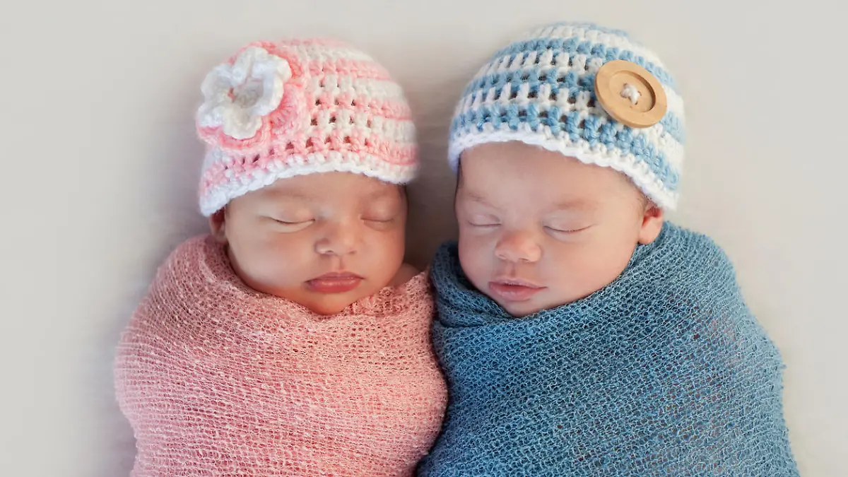 Five week old sleeping boy and girl fraternal twin newborn babies. They are wearing crocheted pink and blue striped hats.