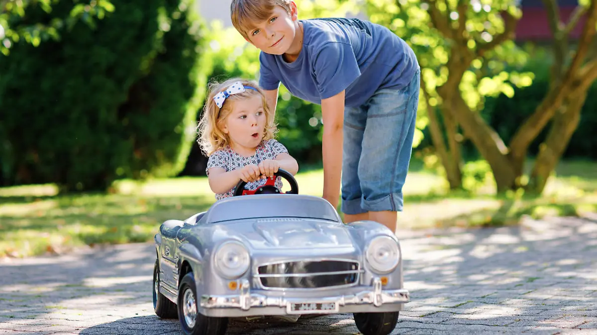 Two happy children playing with big old toy car in summer garden, outdoors. Boy driving car with little girl, cute sister inside. Laughing and smiling kids. Family, childhood, lifestyle concept